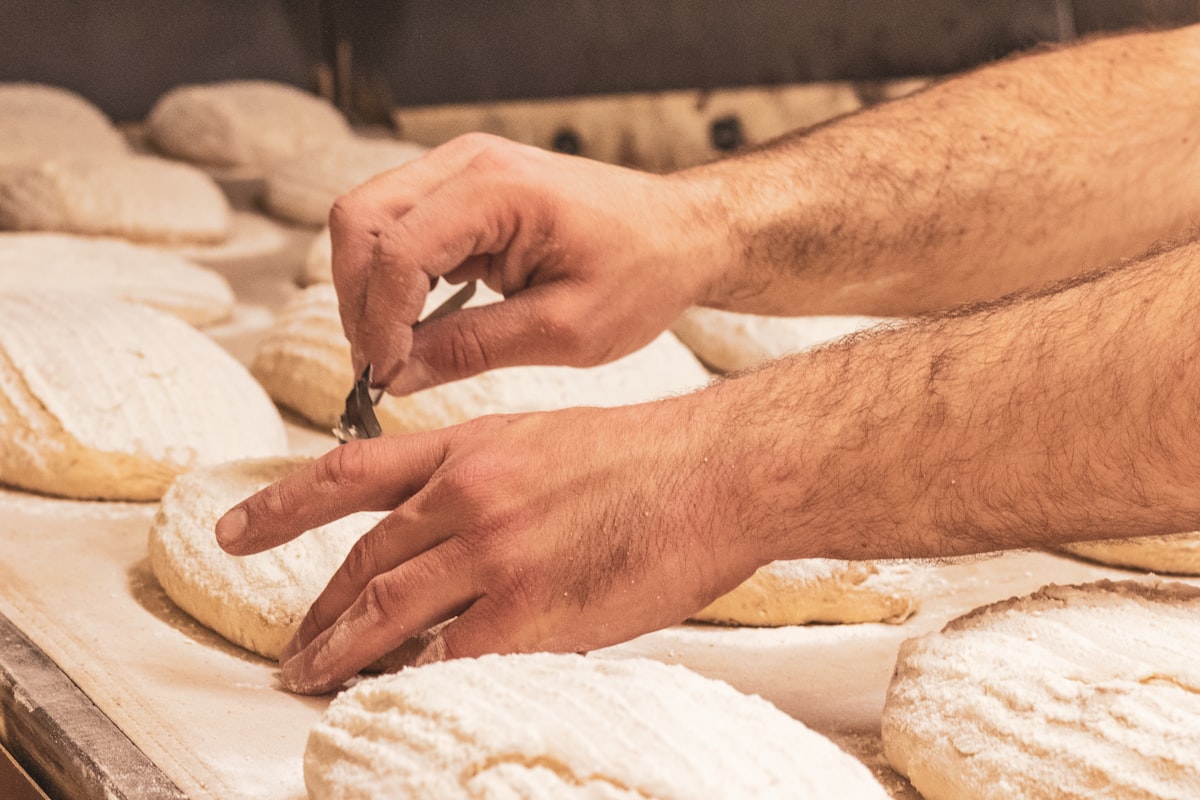 Hände schneiden Teiglinge vor dem Backen ein